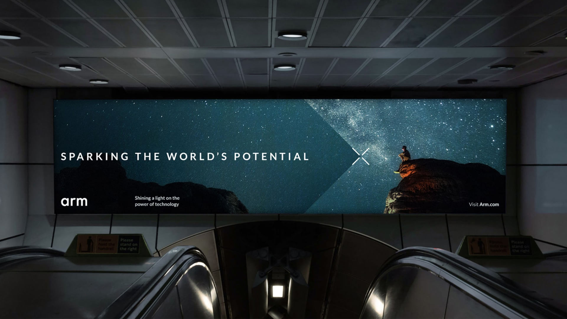 A large screen at the top of an escalator showing an advert for Arm