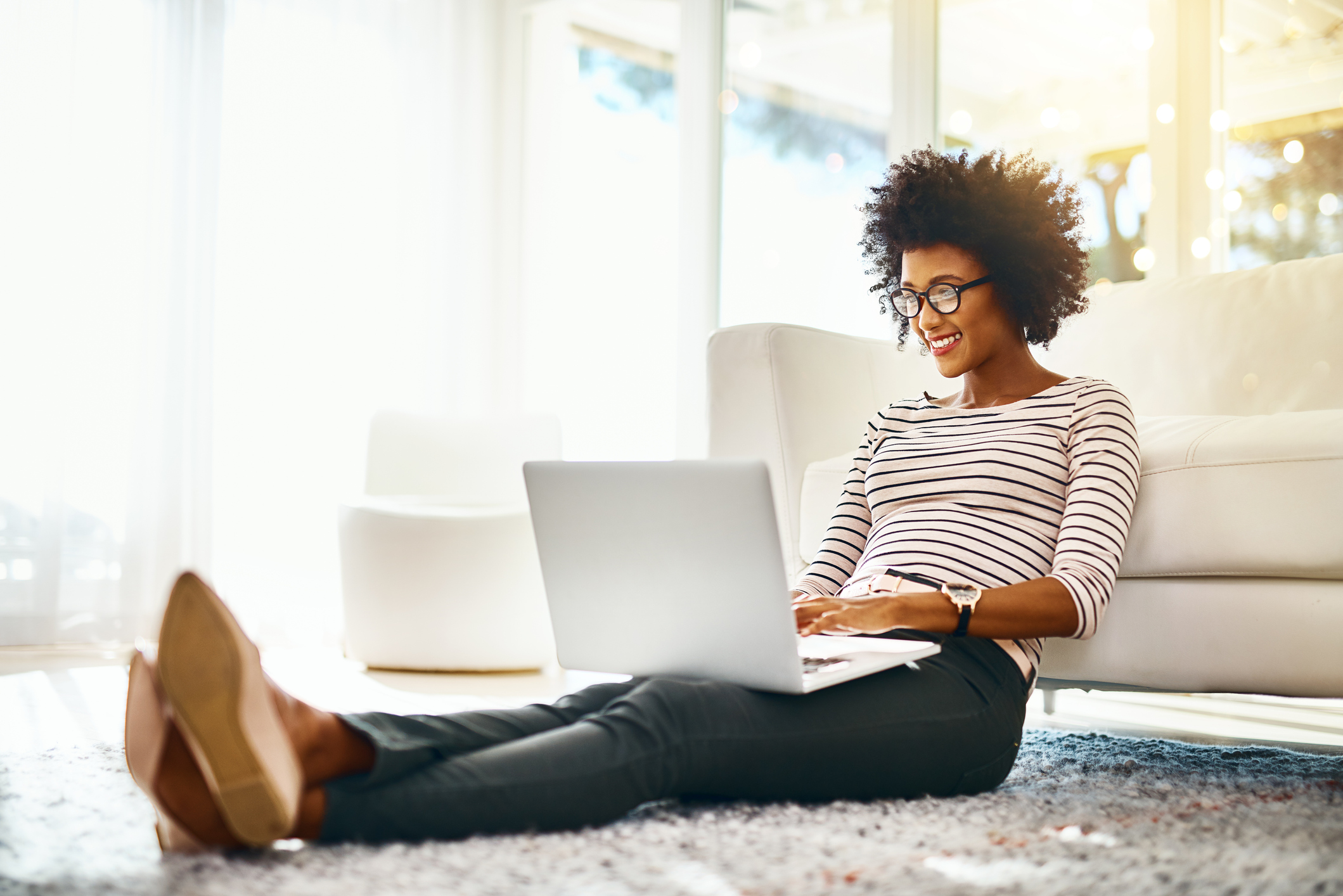 Smiling person sitting on the floor with a laptop sitting in their lap.